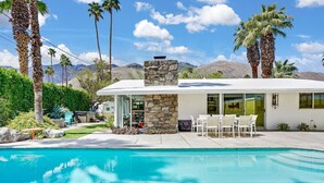 A modern house with a stone fireplace, a pool, and a patio with outdoor furniture. - Twin Palms: Mid-Century Modern with Heated Pool (Palm Springs)