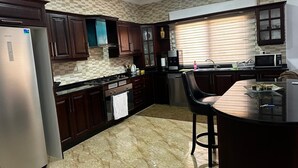 A modern kitchen with dark wooden cabinets, a stainless steel refrigerator, a built-in oven, and a bar area with stools.