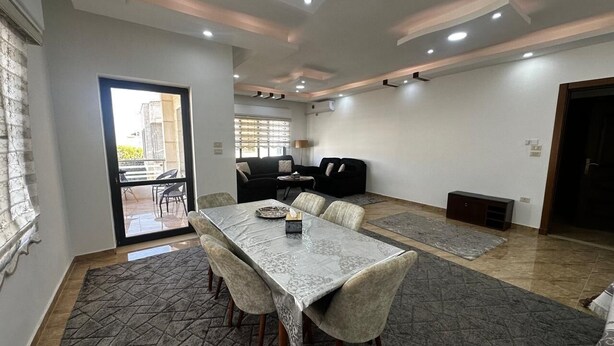 A spacious room with a dining table, chairs, a sofa, and a small TV.