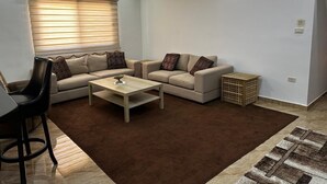 A modern living room with a beige sofa set, a coffee table, and a dining area with a black chair.