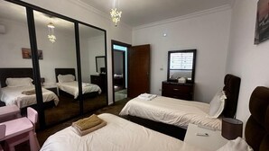 A hotel room with two beds, a desk, a chair, a mirror, a dresser, and a television.