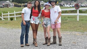 Four people standing on a gravel path with a white fence and houses in the background. - Walk to Rock The South Tent/Car Camping (Cullman)
