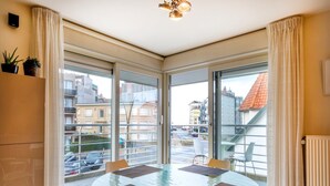 A modern dining area with a glass table, four chairs, and a view of the city through large windows.