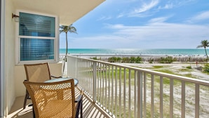 Ein Balkon mit Korbstühlen und Blick auf den Strand, sowie eine Palme.