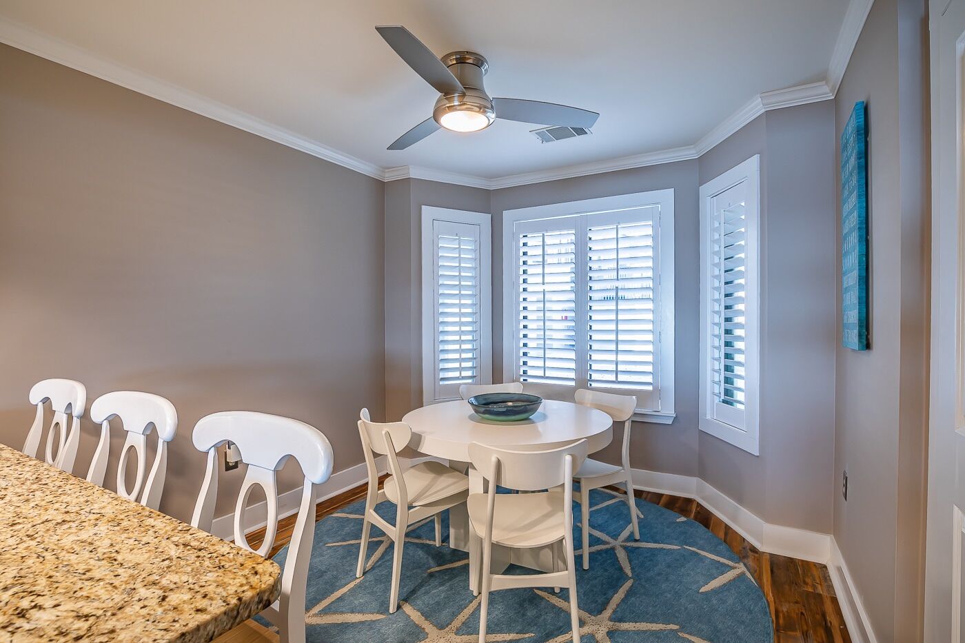 A dining area with a round table, white chairs, and a ceiling fan.