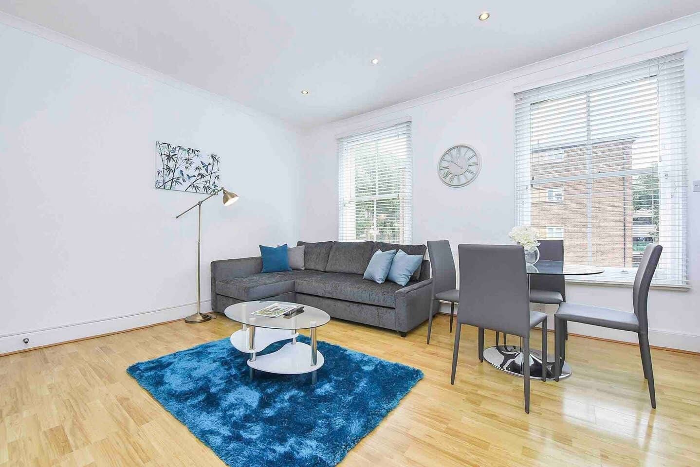 Een moderne woonkamer met een grijze bank, een ronde salontafel en een blauw vloerkleed.