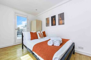 A bedroom with a bed, pillows, a blanket, and artwork on the wall.
