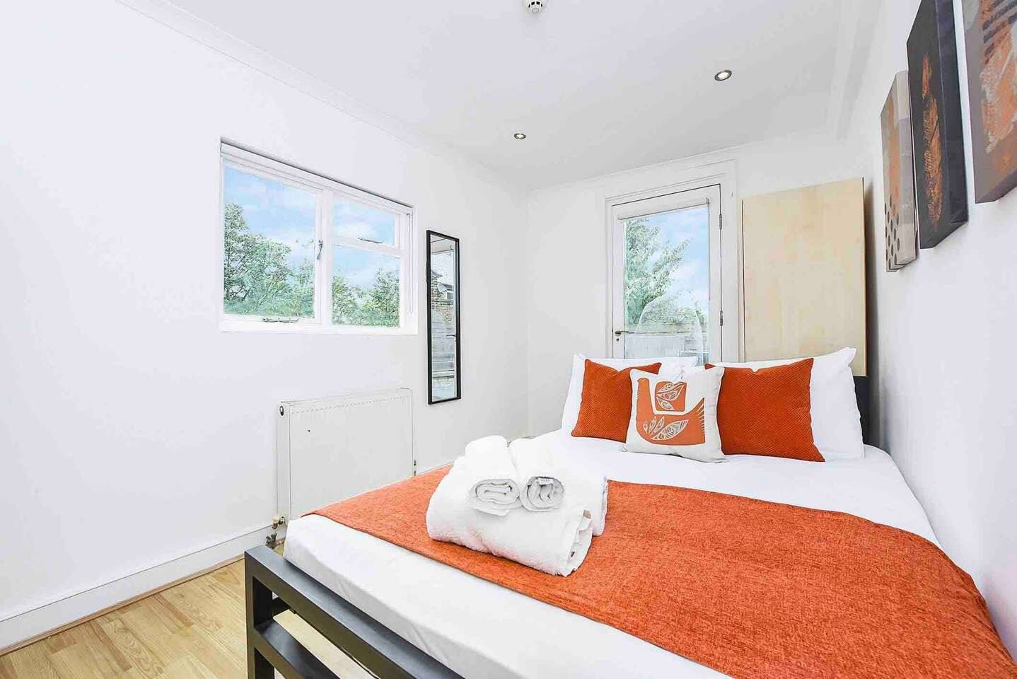 A bedroom with a bed, two windows, a radiator, and artwork on the wall.