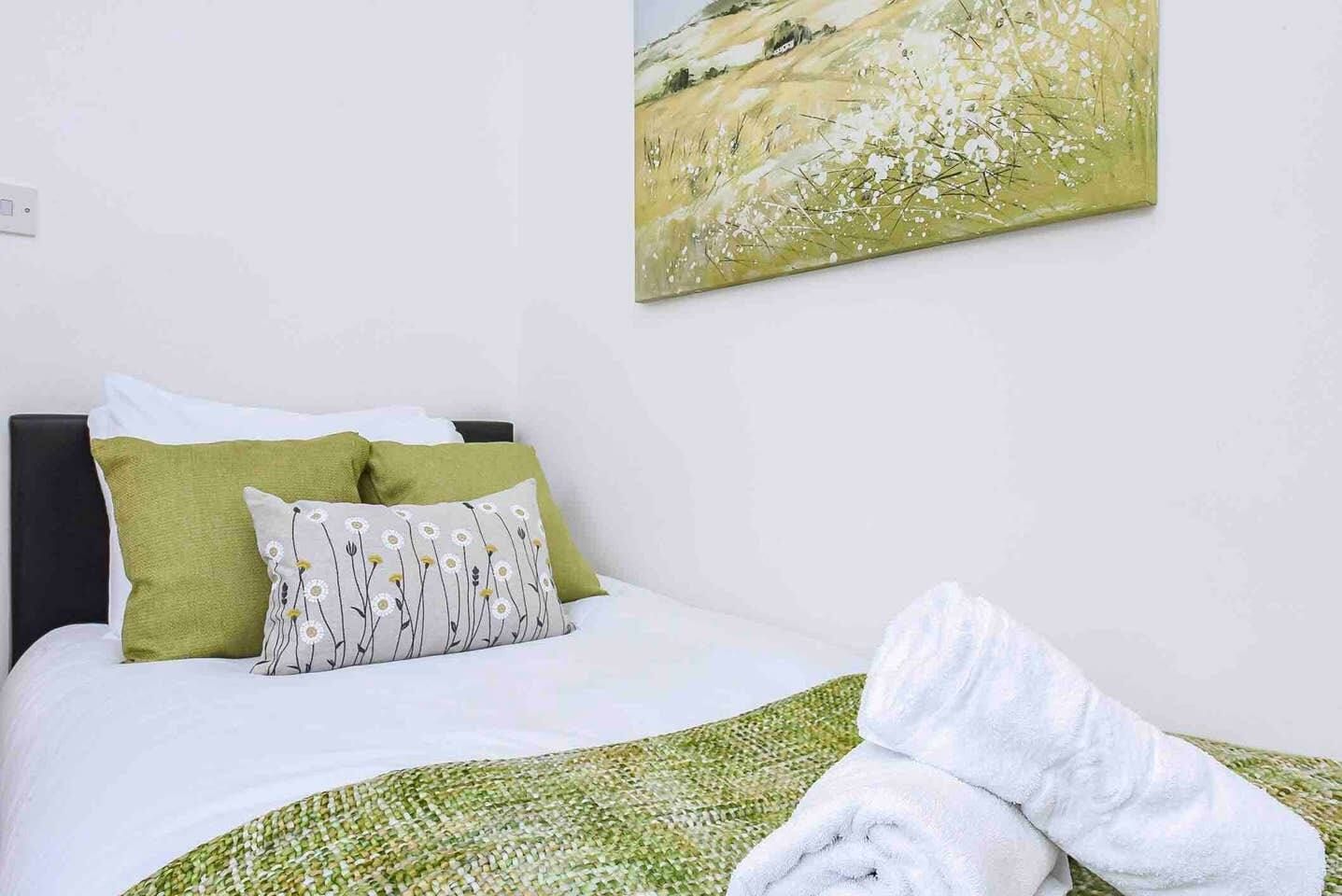 Un lit bien fait, avec des oreillers verts et blancs, une couverture blanche et une serviette blanche roulée posée sur le lit.