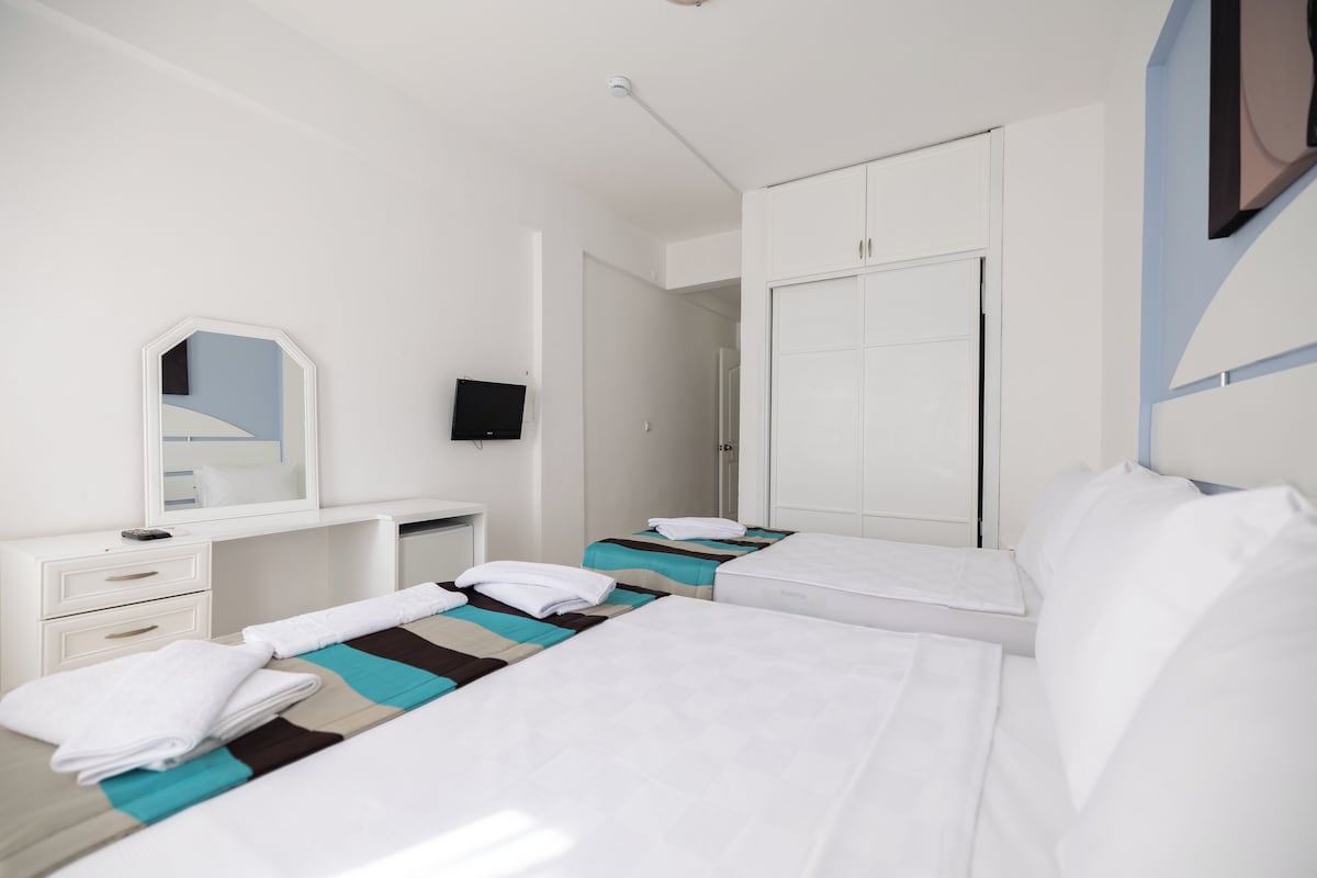 Habitación de hotel con dos camas, un escritorio con silla, un espejo, un armario y un televisor.