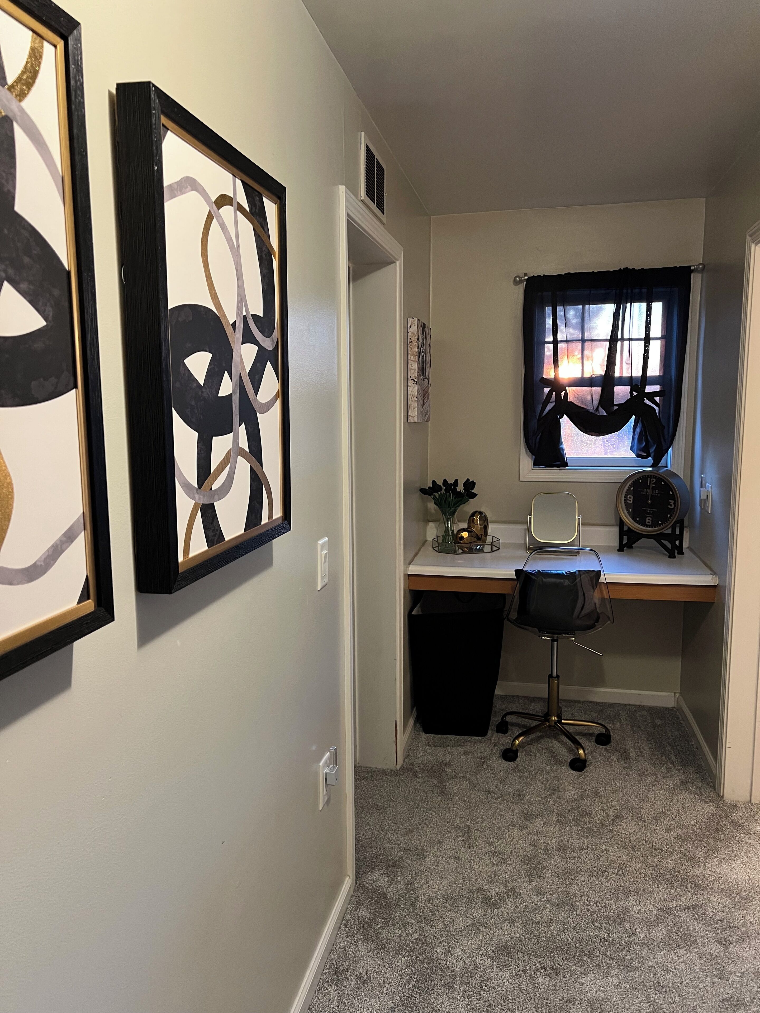 A small office space with a desk, chair, and two framed abstract artworks on the wall.