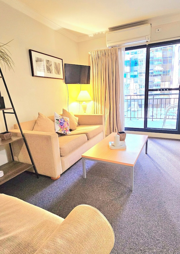 Una sala de estar con sofá, mesa de centro, televisor y ventana con cortinas.