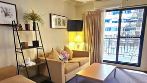 Ein Wohnzimmer mit einer Couch, einem Couchtisch, einem Fernseher, einer Lampe und einem Fenster mit Vorhängen.