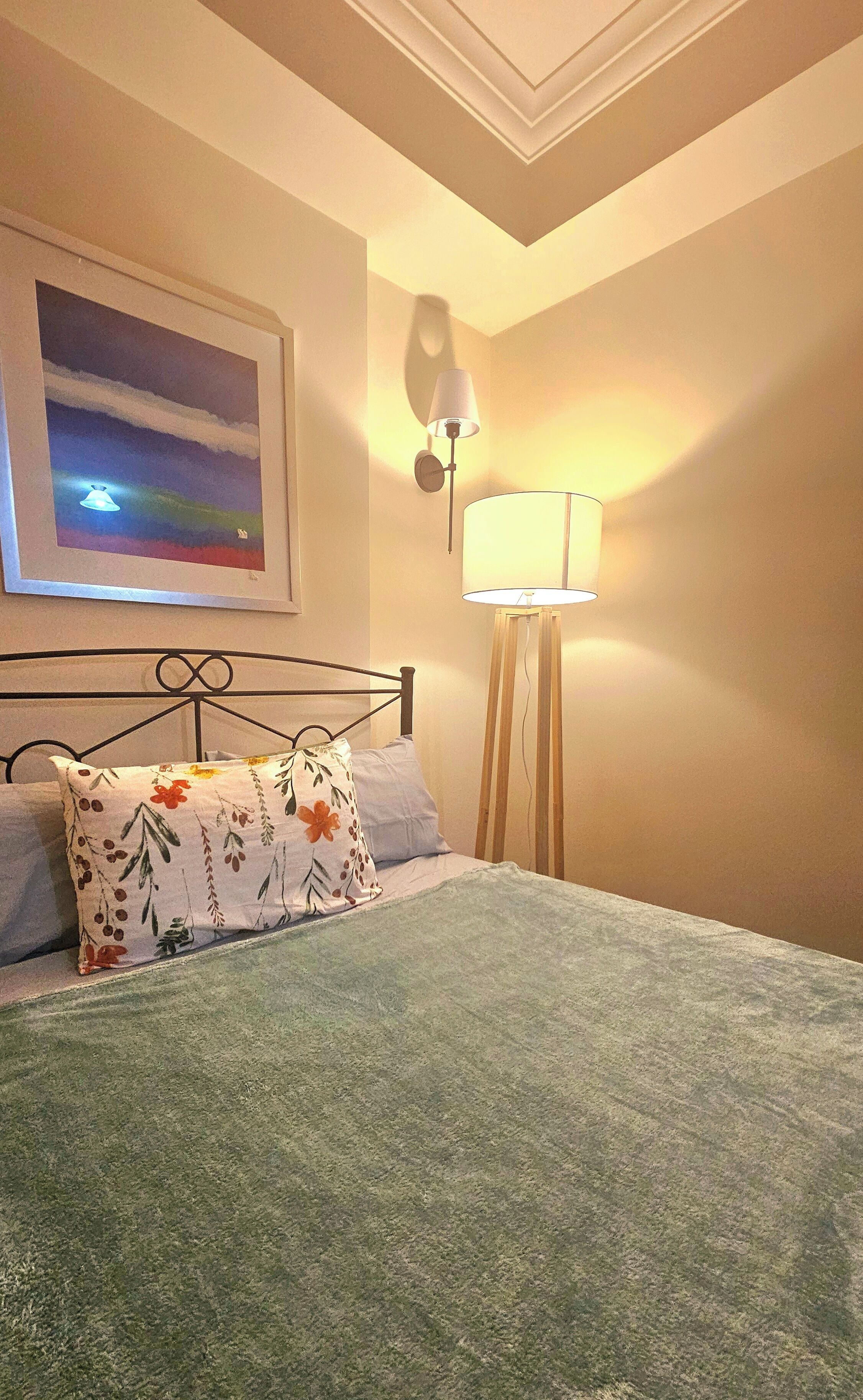 A neatly made bed with floral pillows, a bedside lamp, and a framed picture on the wall.