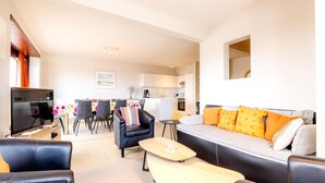 A modern living room with a sofa, chairs, a TV, and a dining area with a table and chairs.