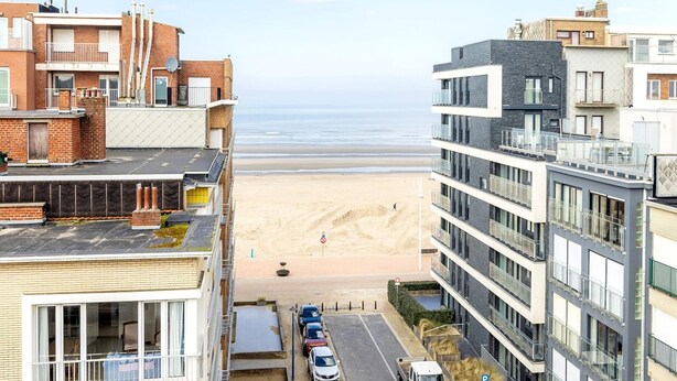 A coastal residential area with modern buildings, a sandy beach, and a clear sky.