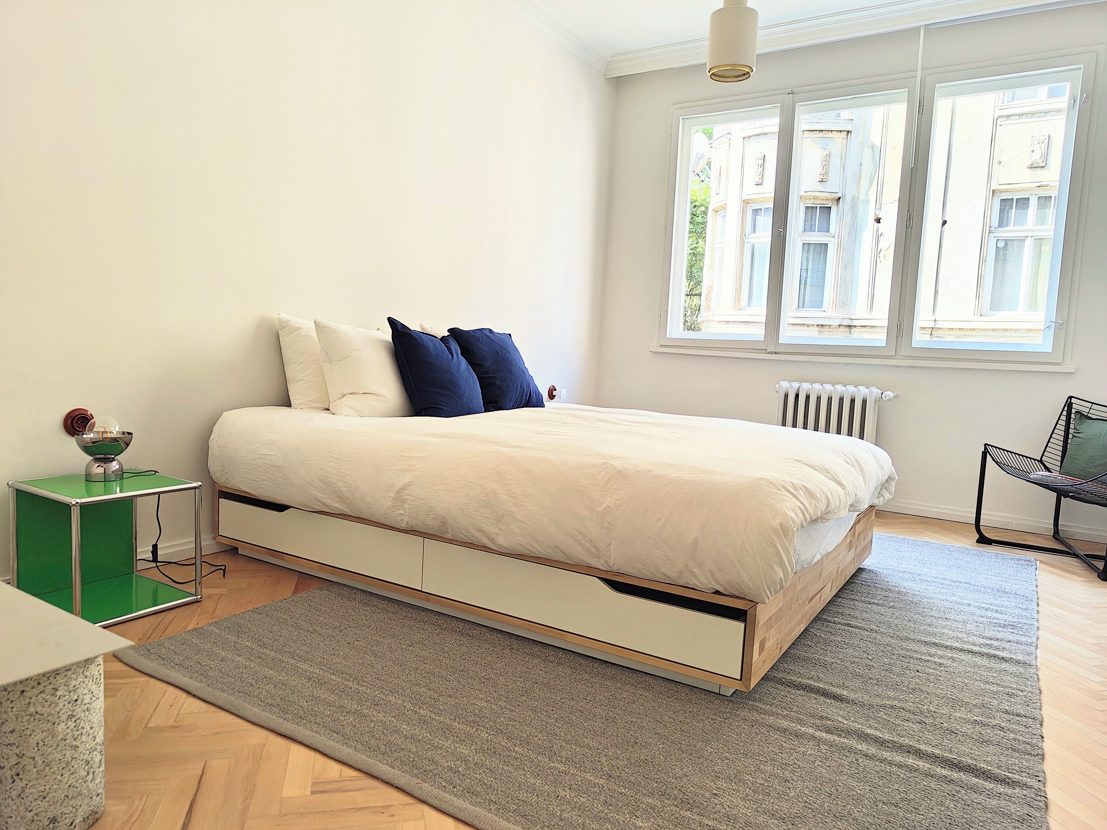 Une chambre à coucher moderne, avec un lit, une table de chevet et une vue sur l’extérieur par une fenêtre.