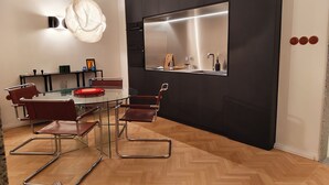 A modern dining area with a glass table, metal chairs, and a black kitchen with stainless steel appliances.