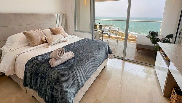 Un dormitorio moderno con una cama grande, un balcón con vistas a la playa y un comedor.