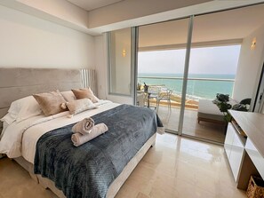 A modern bedroom with a large bed, a balcony with a view of the beach, and a dining area. - Cartagena Beach Resort (Cartagena de Indias)