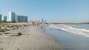 Una playa con costa rocosa, algunas personas y edificios altos al fondo.