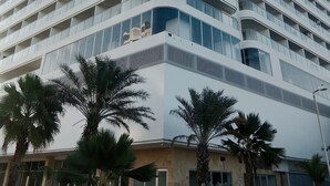 Un hotel alto y moderno con fachada curva, varios balcones y palmeras en primer plano.