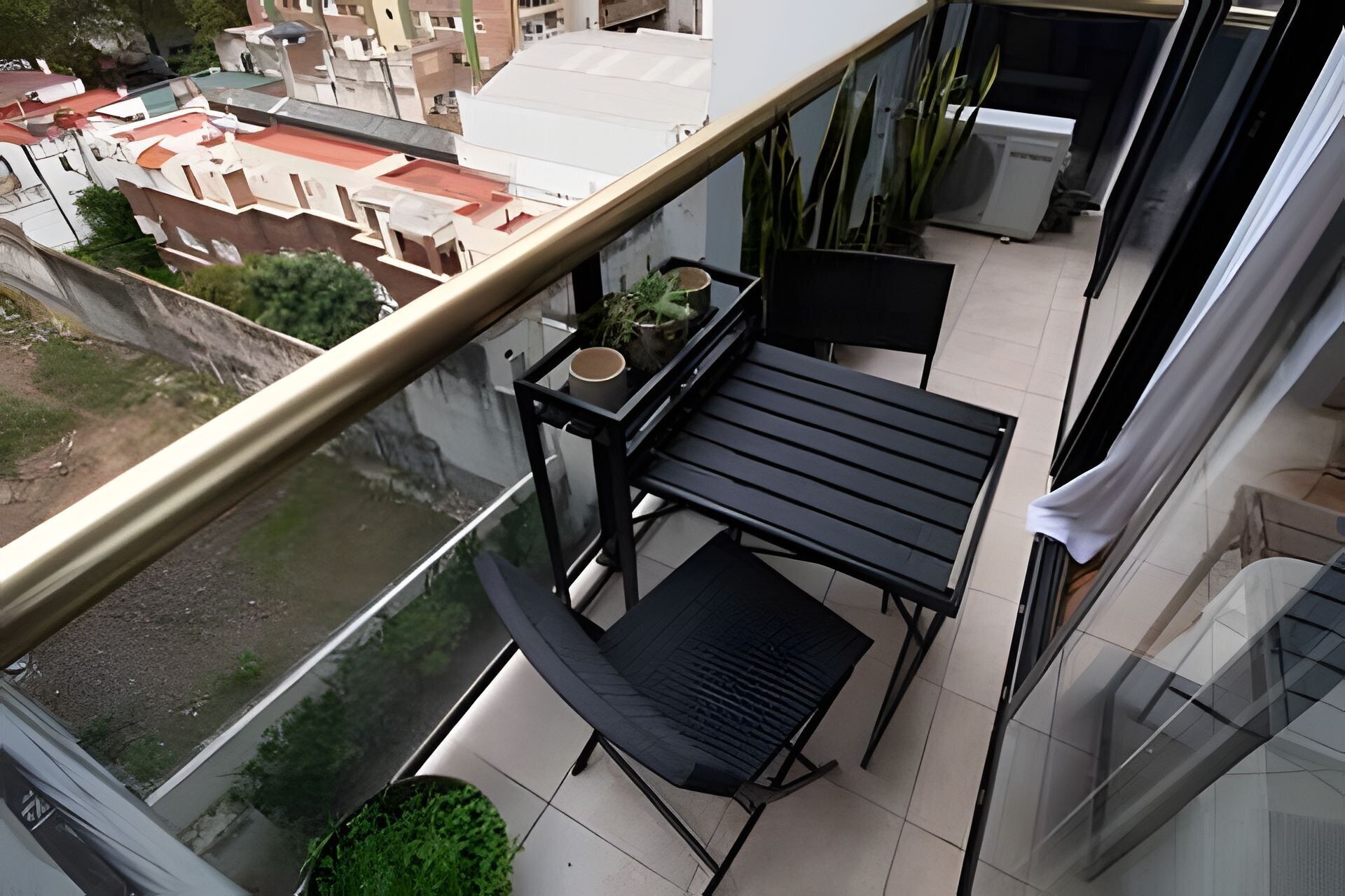 A balcony with a table and chairs, a potted plant, and a view of the cityscape.