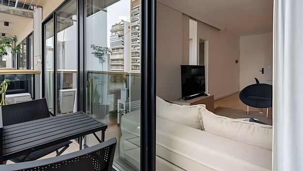 A modern living room with a sofa, a TV, and a dining area with a table and chairs. - King Suite in Recoleta with Pool & Gym (Buenos Aires)