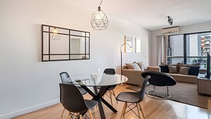 A modern living room with a glass dining table, black chairs, a beige sofa, and a large window with a view of buildings. - King Suite in Recoleta with Pool & Gym (Buenos Aires)