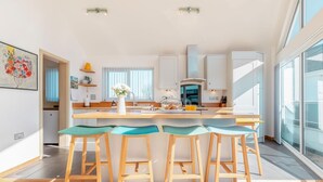 A modern kitchen with a central island, bar stools, and a large window providing natural light. - 4 Bed in Instow (oc-i31748) (Instow)