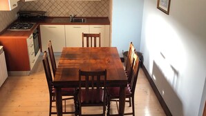 Un comedor con mesa y sillas de madera, una cocina con armarios blancos y salpicadero de azulejos.