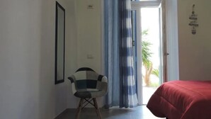 Une pièce avec un lit, une chaise, une porte avec des rideaux et une petite plante à l’extérieur.