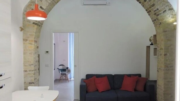 Un salon avec un canapé gris foncé, des coussins rouges, une table blanche et un tapis rouge.