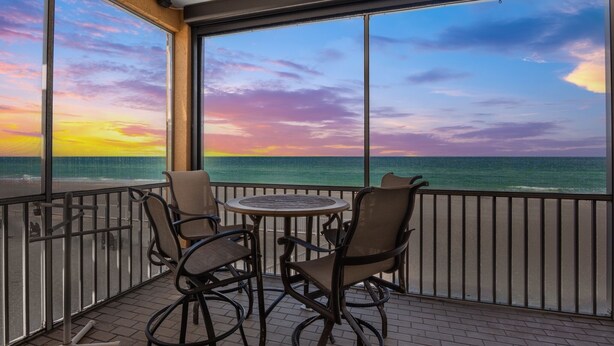 Ein Balkon mit Tisch und Stühlen mit Blick auf einen Sonnenuntergang über dem Meer.