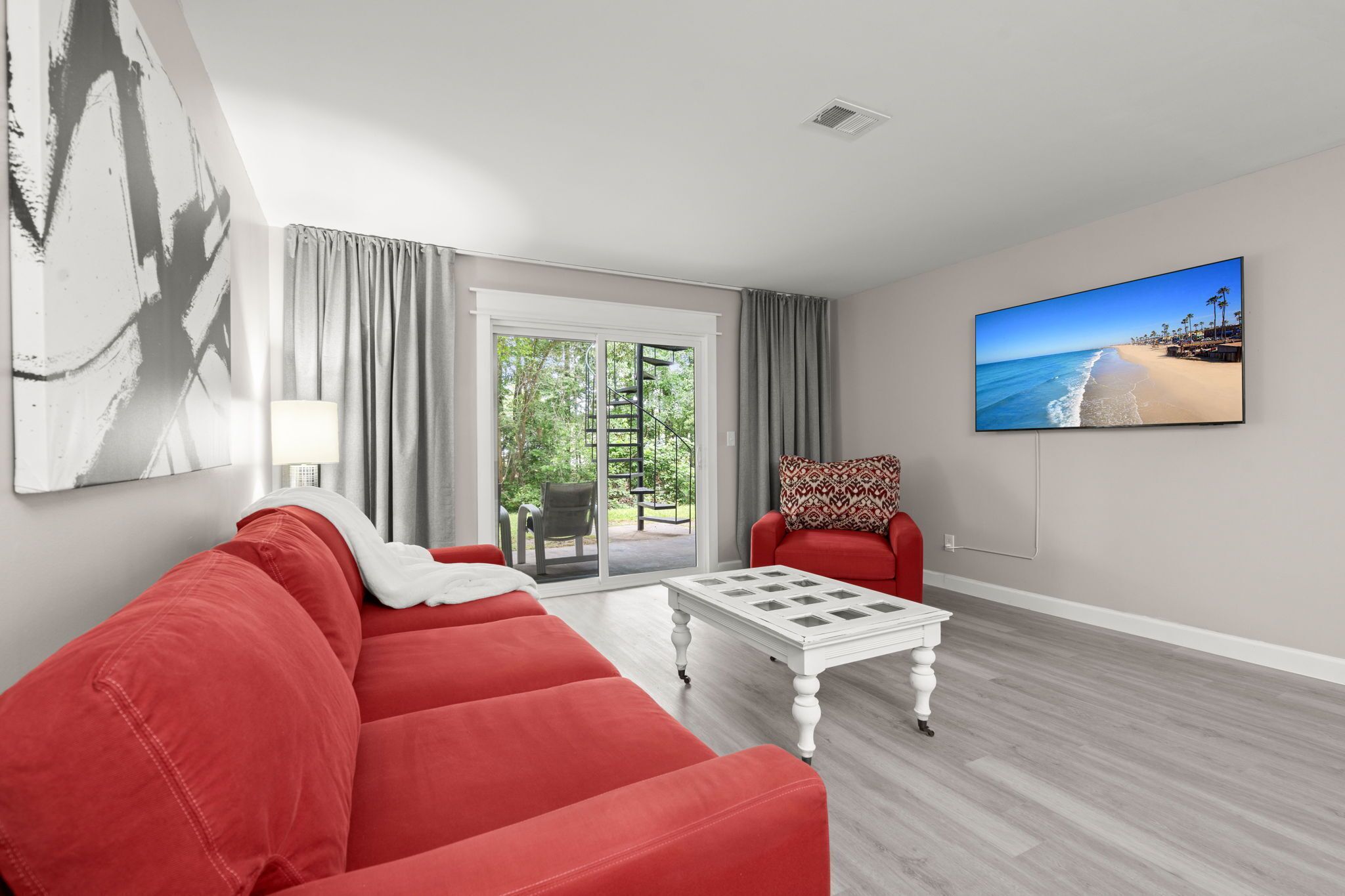 Een moderne woonkamer met een rode bank, een witte bijzettafel en een groot schilderij met uitzicht op het strand.
