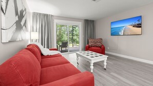 En moderne stue med en rød sofa, et hvidt sofabord og et stort maleri med udsigt til stranden på væggen.