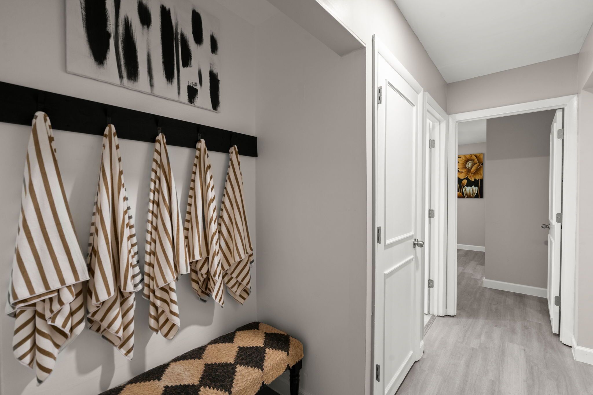 A hallway with striped towels hanging on a rack, a bench, and a door leading to another room.