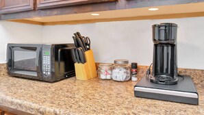 A kitchen counter with a microwave, a coffee maker, a knife block, and spice jars. - Your Perfect Private HideAway (Houston)