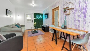 A living room with a sofa, a dining table, and a TV. There is a neon sign on the wall and a green plant. - Your Perfect Private HideAway (Houston)