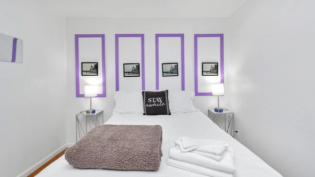 A modern hotel room with a large bed, two nightstands, a fluffy throw blanket, and a pillow with "STAY awhile" text. - Your Perfect Private HideAway (Houston)