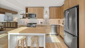A modern kitchen with wooden cabinets, stainless steel appliances, and a central island with stools.