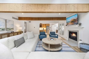 Uma sala de estar moderna com sofá, cadeiras, mesa de centro, lareira e televisão.
