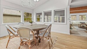 A spacious dining area with a round table, wicker chairs, and a chandelier.