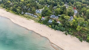 An aerial view of a coastal area with a sandy beach, dense greenery, and residential buildings.