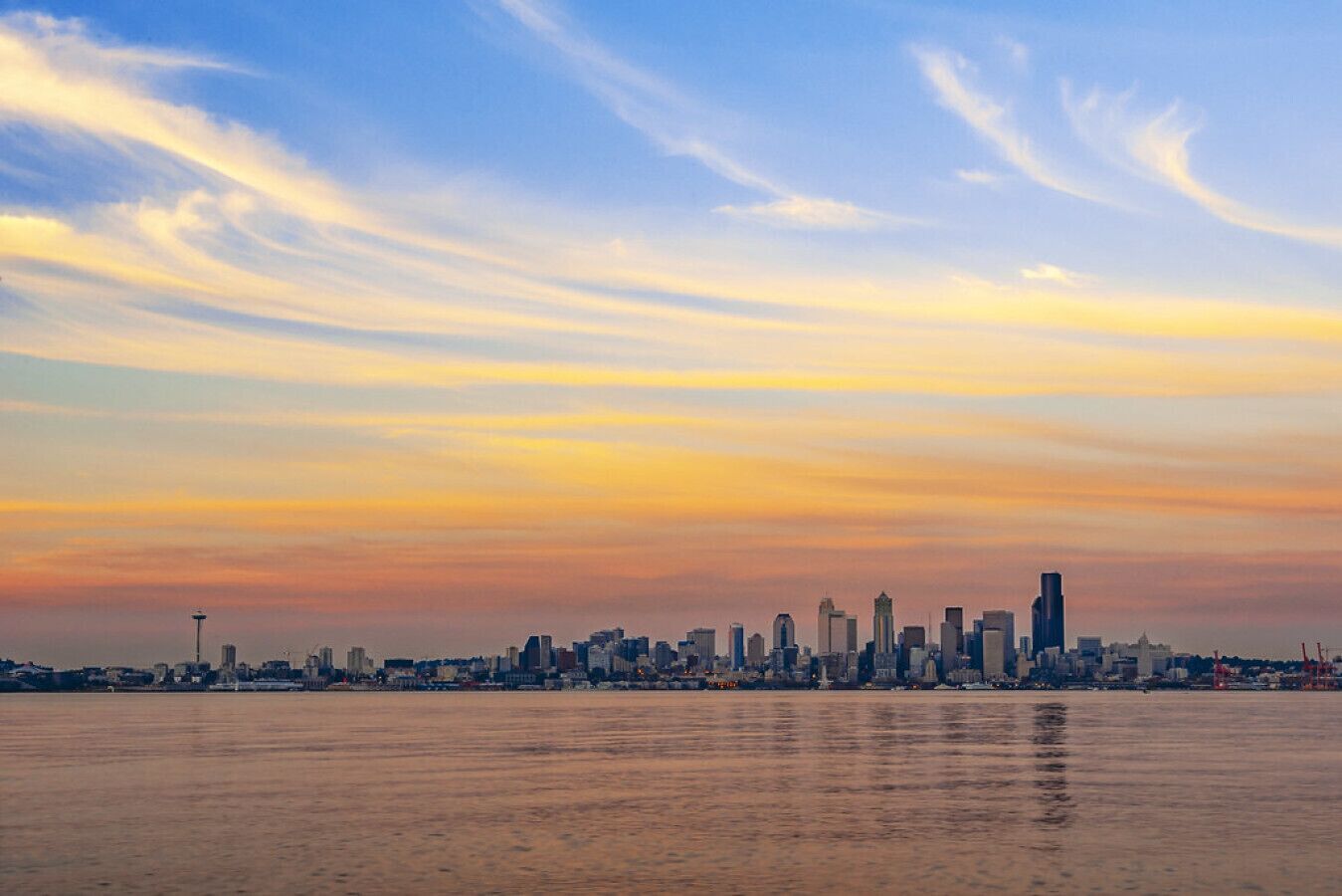 Une vue sur les gratte-ciel d’une ville au coucher du soleil, avec une étendue d’eau au premier plan.
