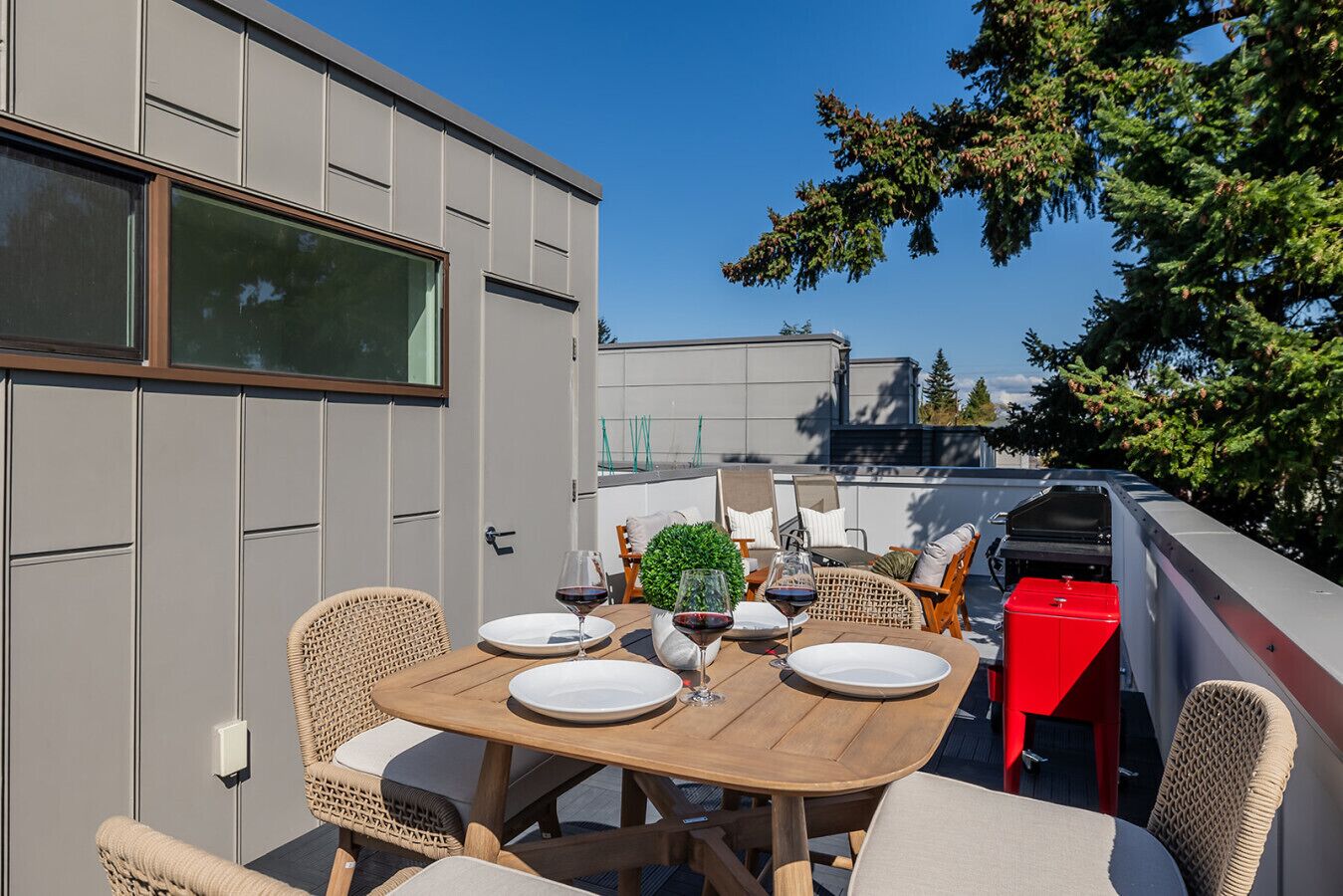Terraza en la azotea con una mesa de madera dispuesta para comer, sillas de mimbre y un cubo de basura rojo.