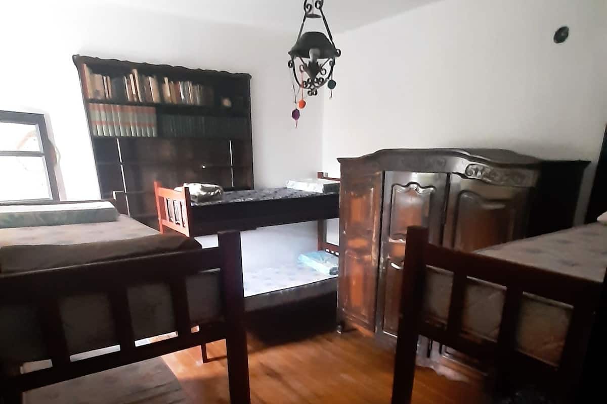 A dining area with a wooden table and chairs, a hanging light fixture, and a bookshelf in the background.