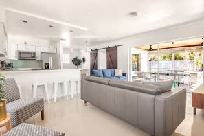 A modern living room with a grey sofa, white chairs, a kitchen area with white cabinets, and a dining area with a table and chairs. - Outdoor Paradise  Heated Pool near Beach 4/3 (Fort Lauderdale)