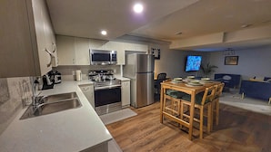 Una cocina moderna con electrodomésticos de acero inoxidable, un comedor con una mesa y sillas de madera, y un televisor de pantalla plana montado en la pared.