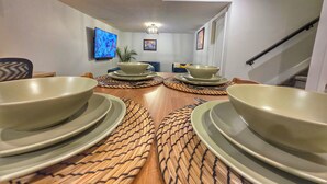 Un comedor con una mesa de madera preparada para cuatro personas, un televisor montado en la pared y una escalera que sube a otro nivel.